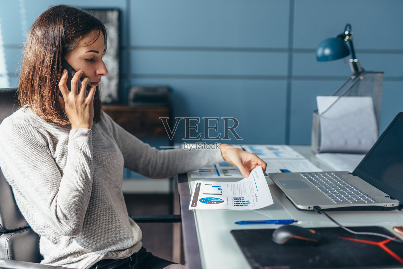 用手机聊天的女人在办公桌前工作。照片摄影图片