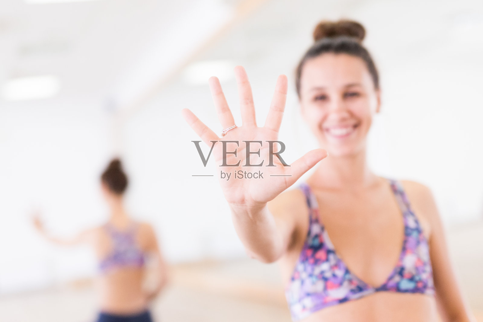 健身运动活跃的女人微笑，穿着时尚运动服显示一个摊开的手掌在瑜伽室的相机。活跃的城市生活方式。照片摄影图片