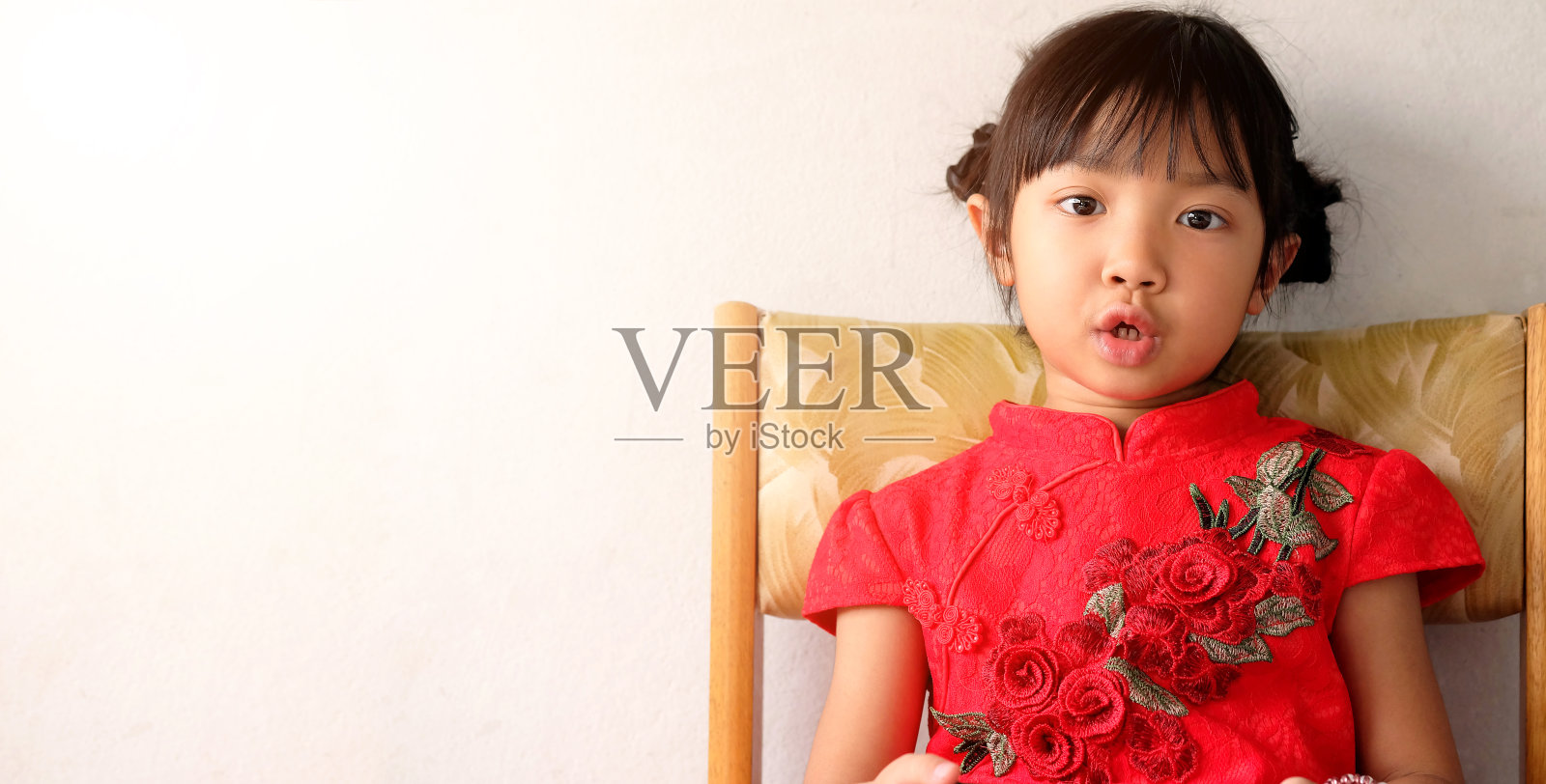 亚洲的小女孩穿着红色的衣裙，坐在白色背景的椅子上，概念服装中国新年，与复制空间照片摄影图片