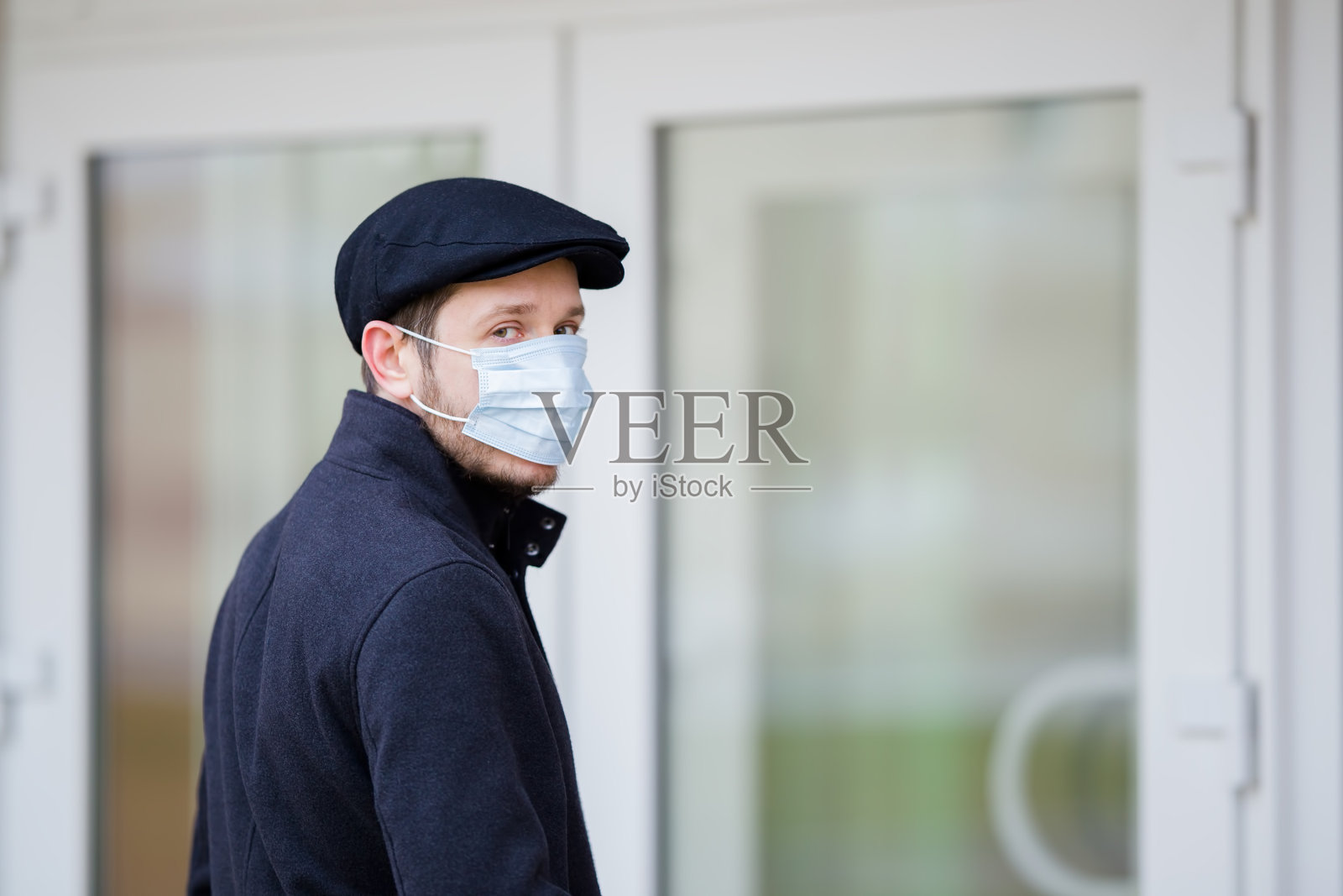 一名年轻男子穿着黑色外套和帽子，戴着口罩捂住口鼻。在隔离期间访问不同机构。第一个保护。医疗保健的概念。特写镜头。照片摄影图片