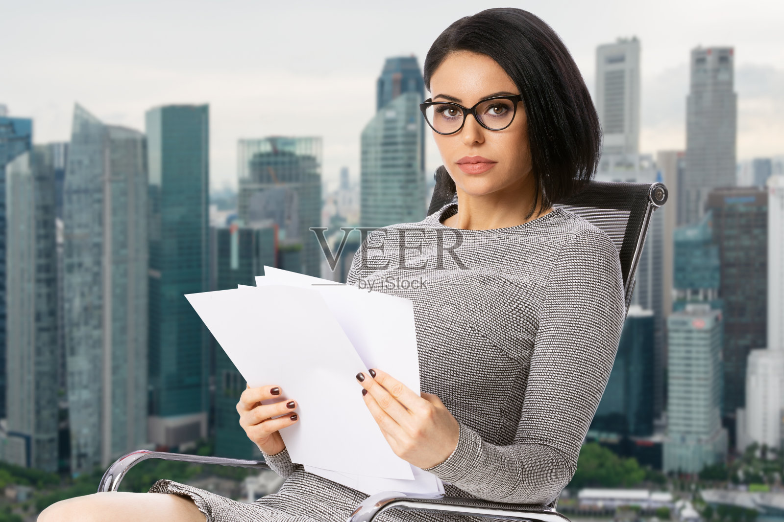 沉思的年轻女商人戴着眼镜坐在椅子上与纸文件在新加坡城市背景。成就商业职业理念。照片摄影图片