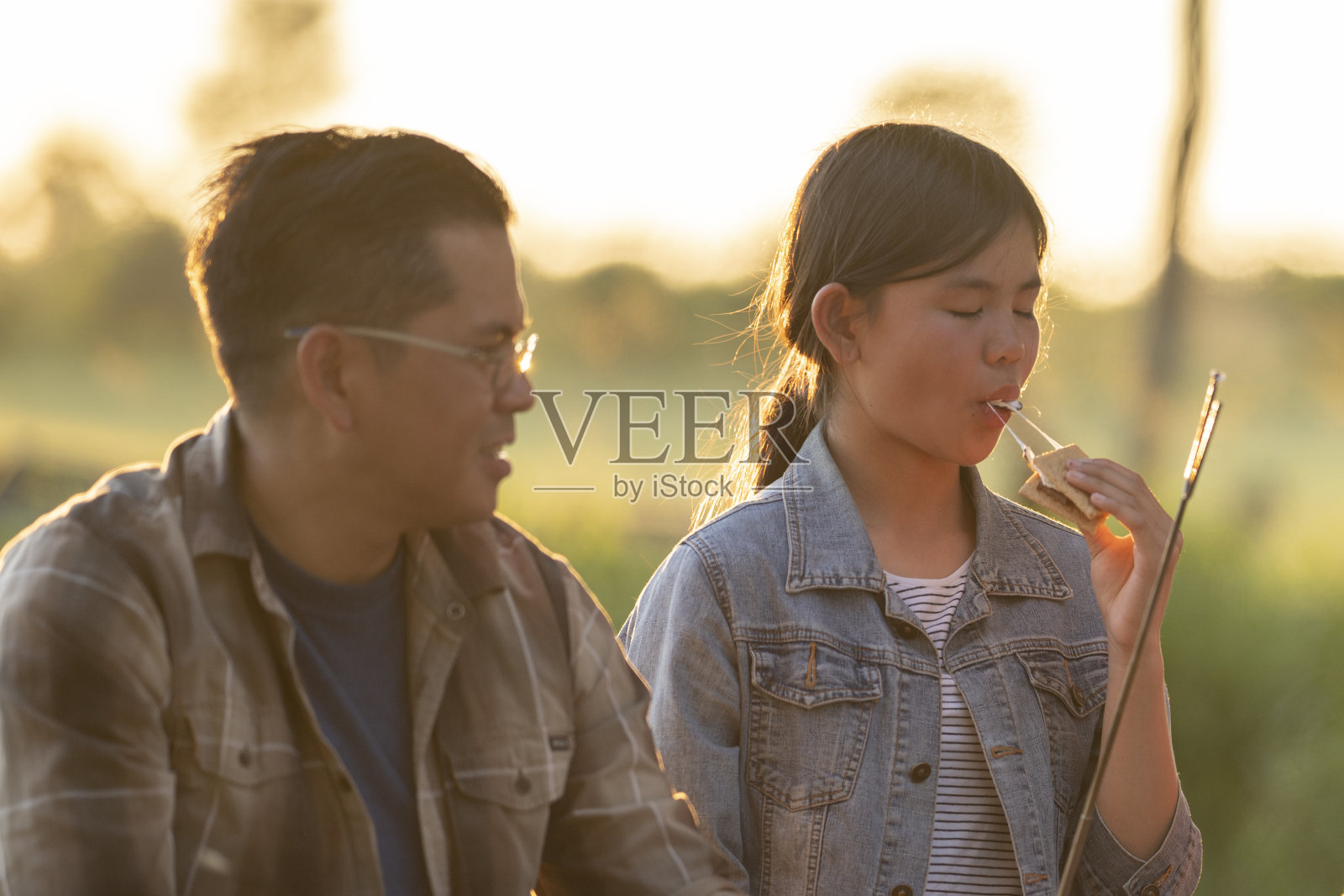 年轻的亚洲家庭围着篝火烤棉花糖照片摄影图片
