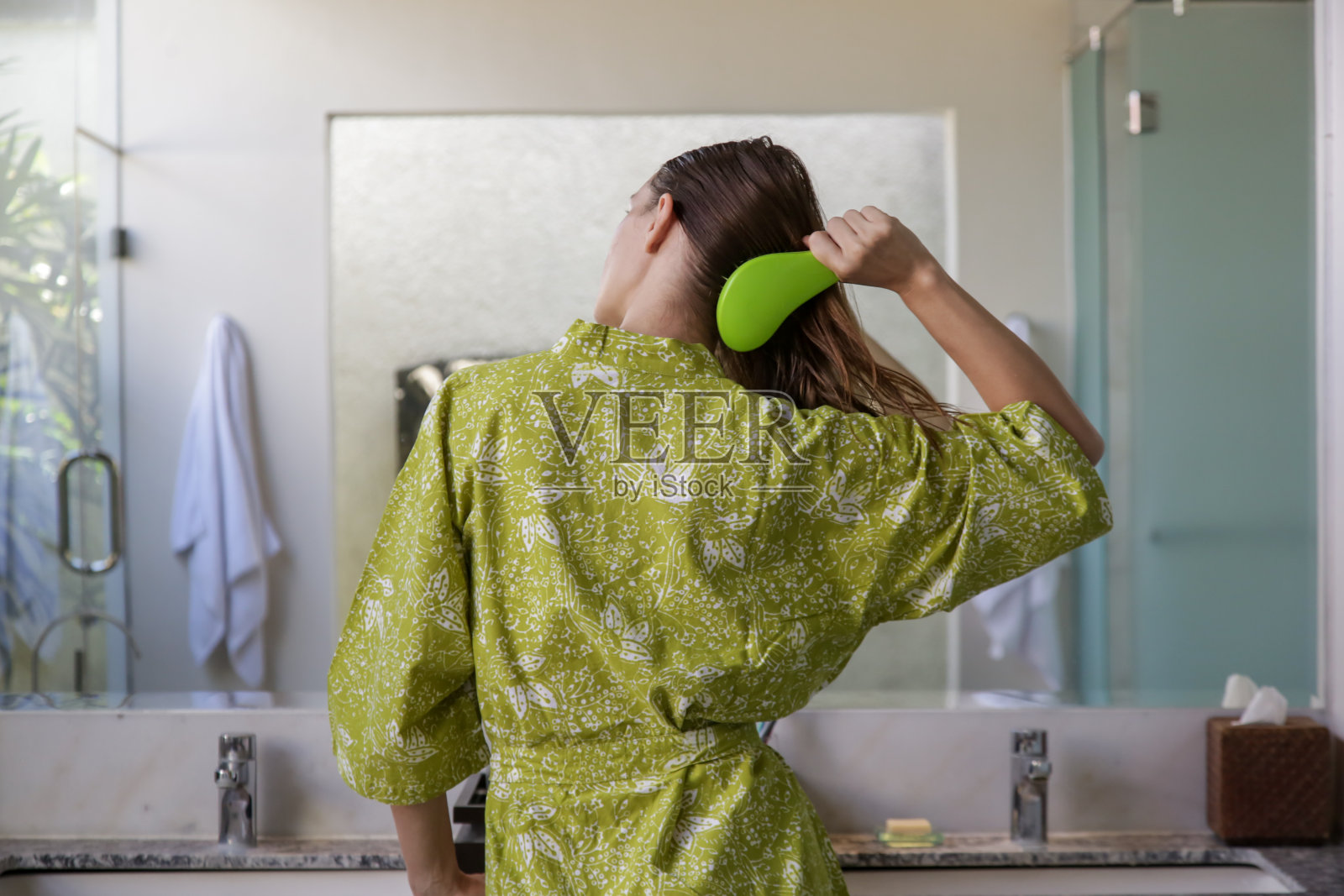 头发护理。在浴室镜子前用塑料梳头刷梳头的黑发女人是罕见的。照片摄影图片