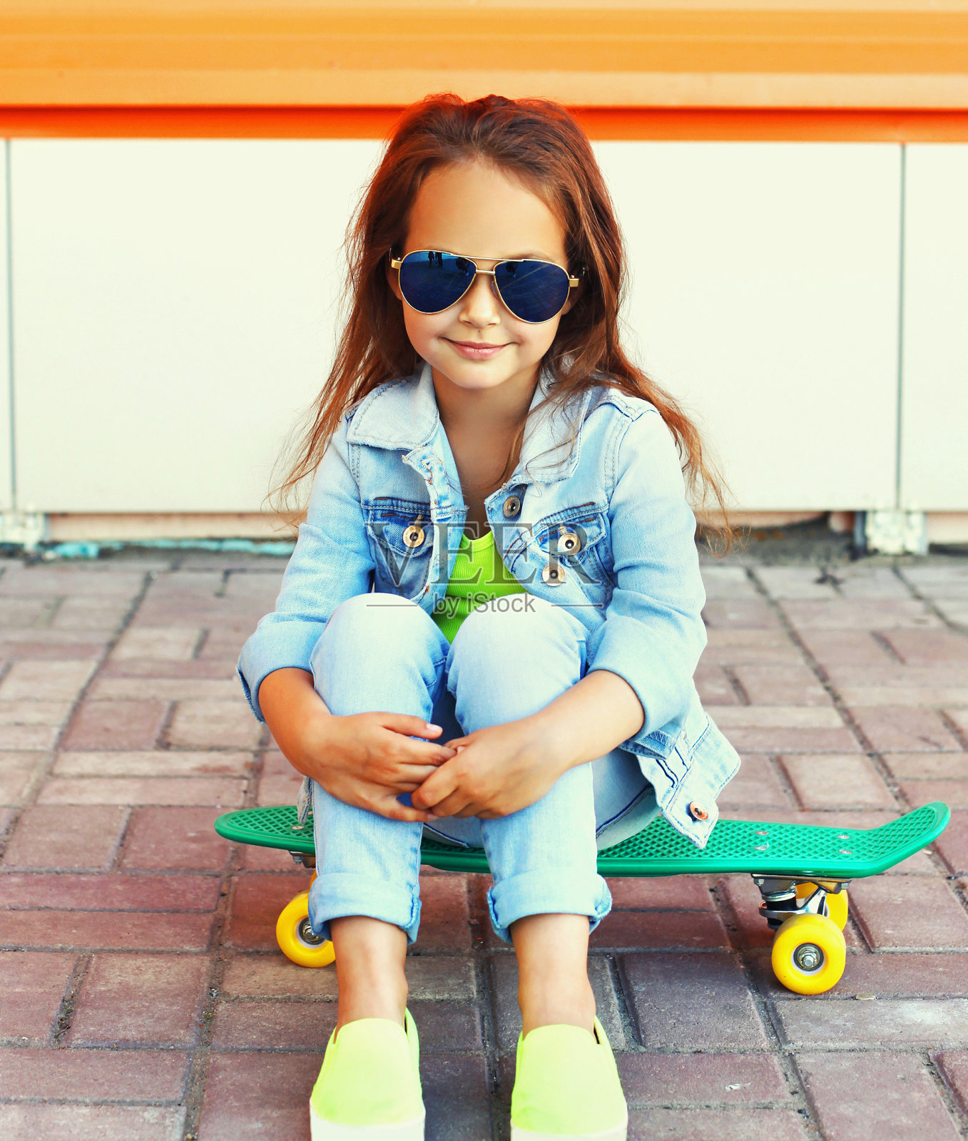 时髦的小女孩坐在绿色滑板上的城市街道照片摄影图片