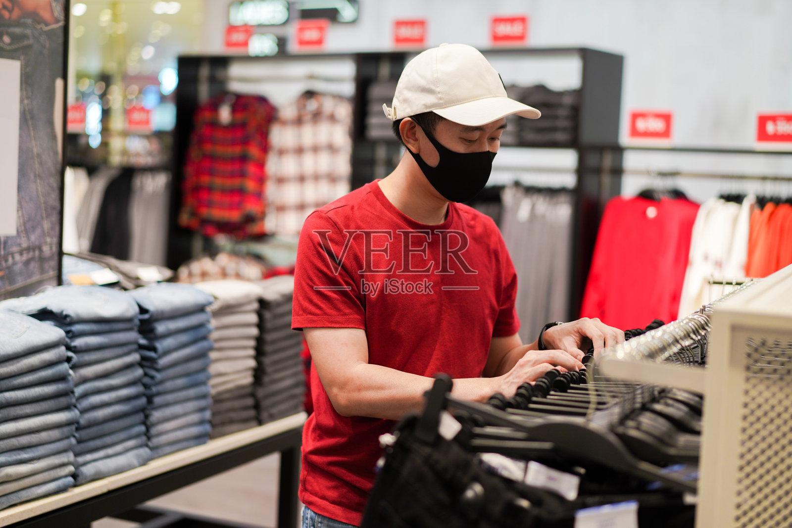 年轻的亚洲男子戴着白色的帽子和黑色的面罩在购物中心买衣服。保护冠状病毒和空气污染照片摄影图片