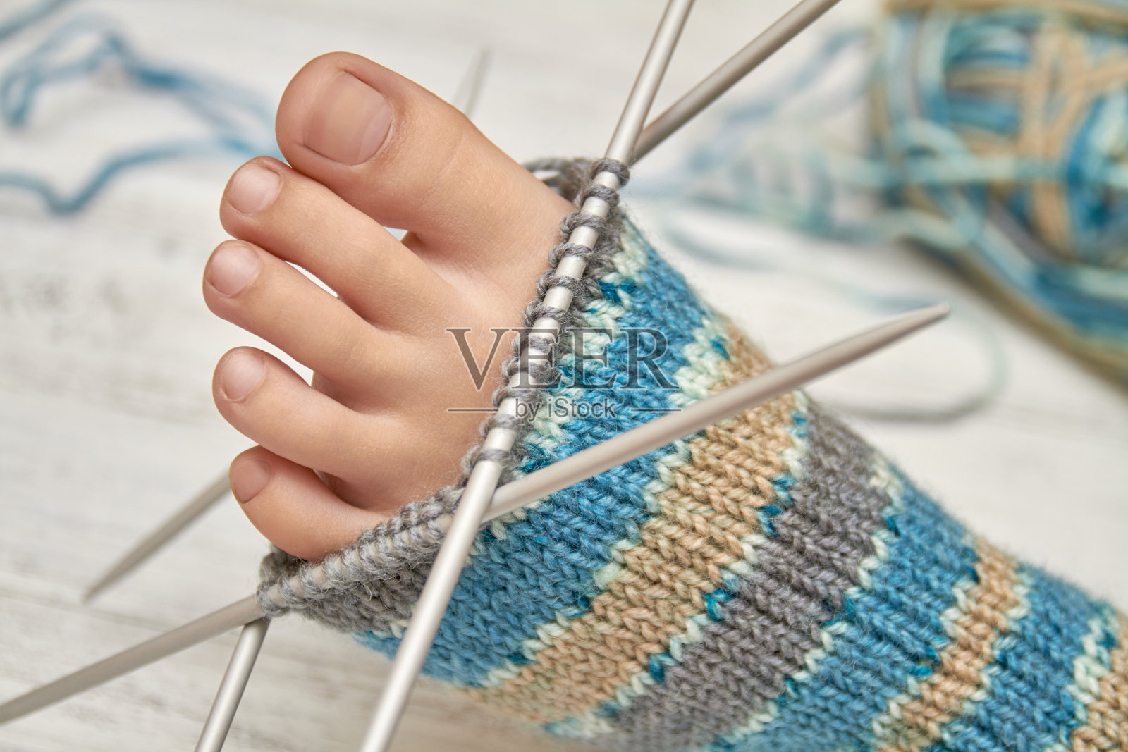 织毛衣时给婴儿脚穿上袜子。浅色木质背景，选择性聚焦照片摄影图片