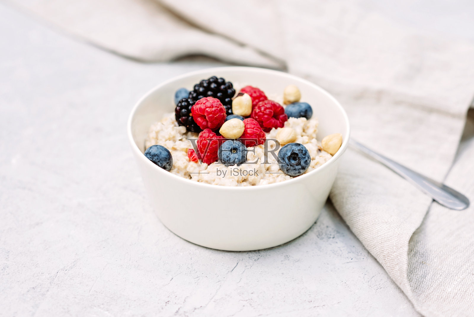 在灰色混凝土背景下，搭配覆盆子、蓝莓、黑莓和坚果的燕麦粥。健康健康的早餐。照片摄影图片