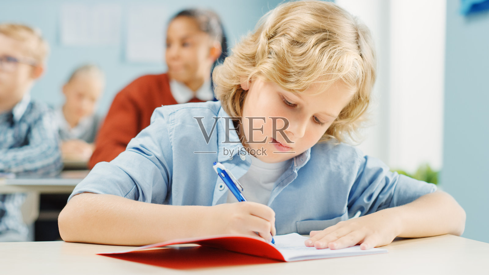 小学课堂:一个聪明可爱的白人男孩在练习笔记本上写字的肖像。初中教室与多元的聪明的孩子们努力工作，学习新东西照片摄影图片