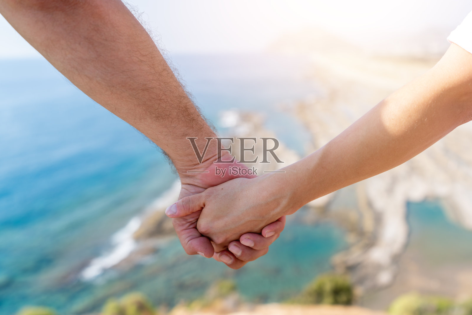 两只手牵着模糊的阳光和美丽的风景一处悬崖和大海。照片摄影图片