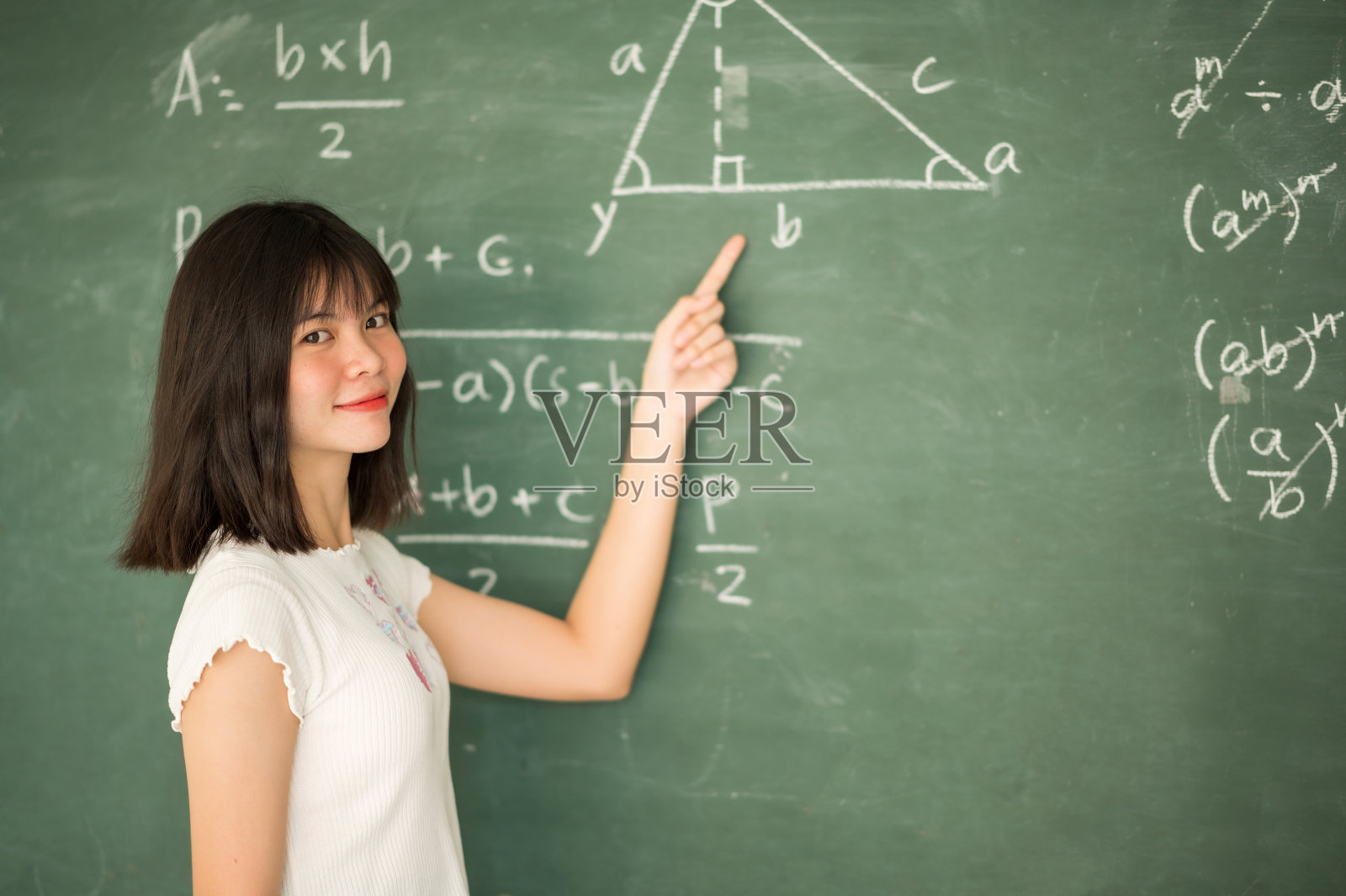 一位亚洲女学生站在教室的黑板前。照片摄影图片