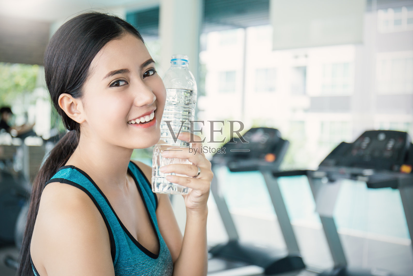 亚洲年轻女子在运动俱乐部运动后喝水，亚洲运动员在健身房喝一瓶水。运动和保健理念照片摄影图片