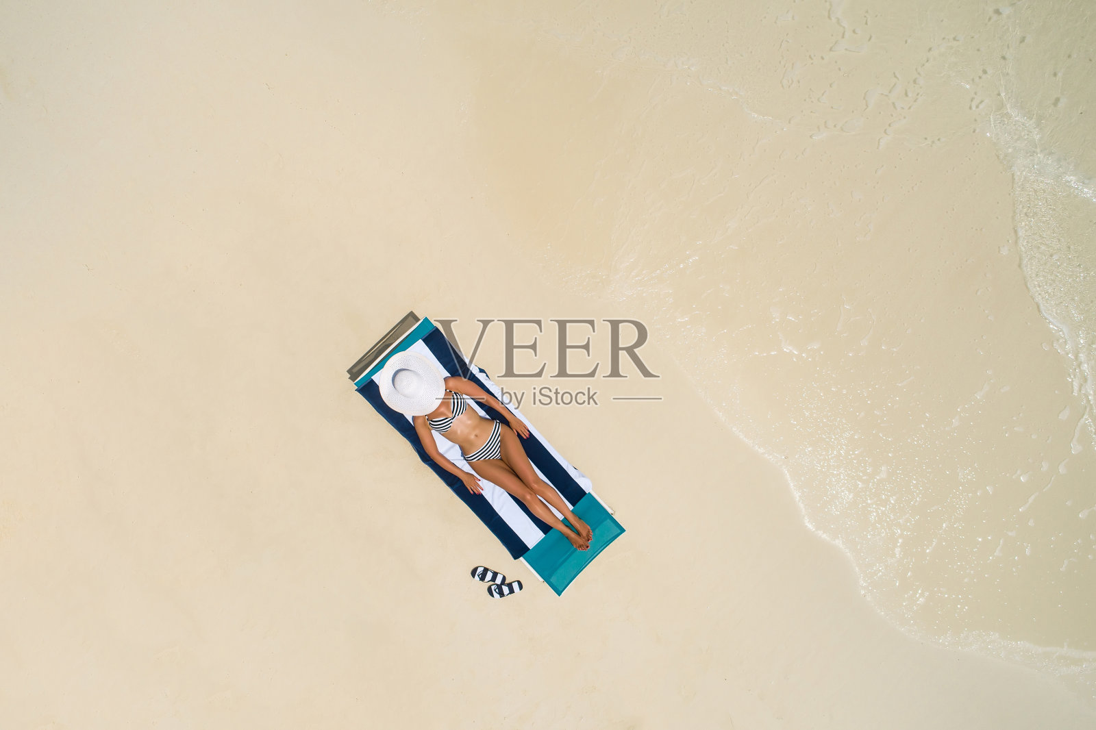 鸟瞰图，一个苗条的女人躺在马尔代夫的沙滩椅上晒太阳。夏日的海景带着少女，美丽的海浪，五颜六色的水。俯视图从无人机。照片摄影图片