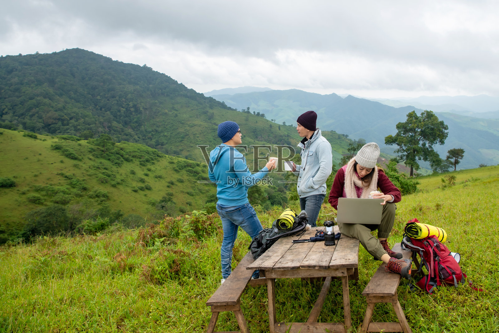 一群亚洲男女朋友喜欢在秋天的森林山一起徒步旅行和喝咖啡。年轻女子使用笔记本电脑在户外上网工作。友谊和假期的概念。照片摄影图片