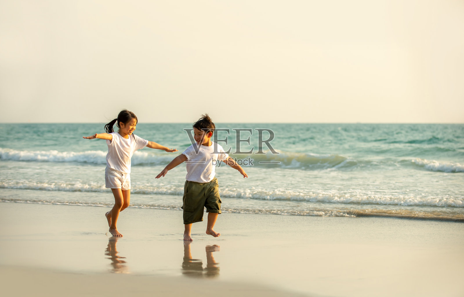 快乐的亚洲家庭小弟弟和小妹妹一起在夏日日落的海滩上奔跑和玩耍。可爱的兄弟姐妹孩子女孩和男孩放松和有乐趣的户外暑假照片摄影图片