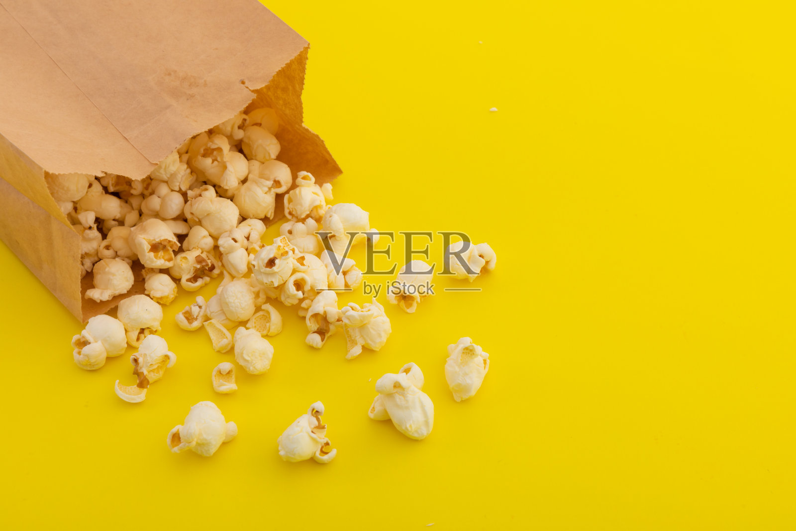 高角度的爆米花溢出的棕色纸袋在黄色的背景照片摄影图片