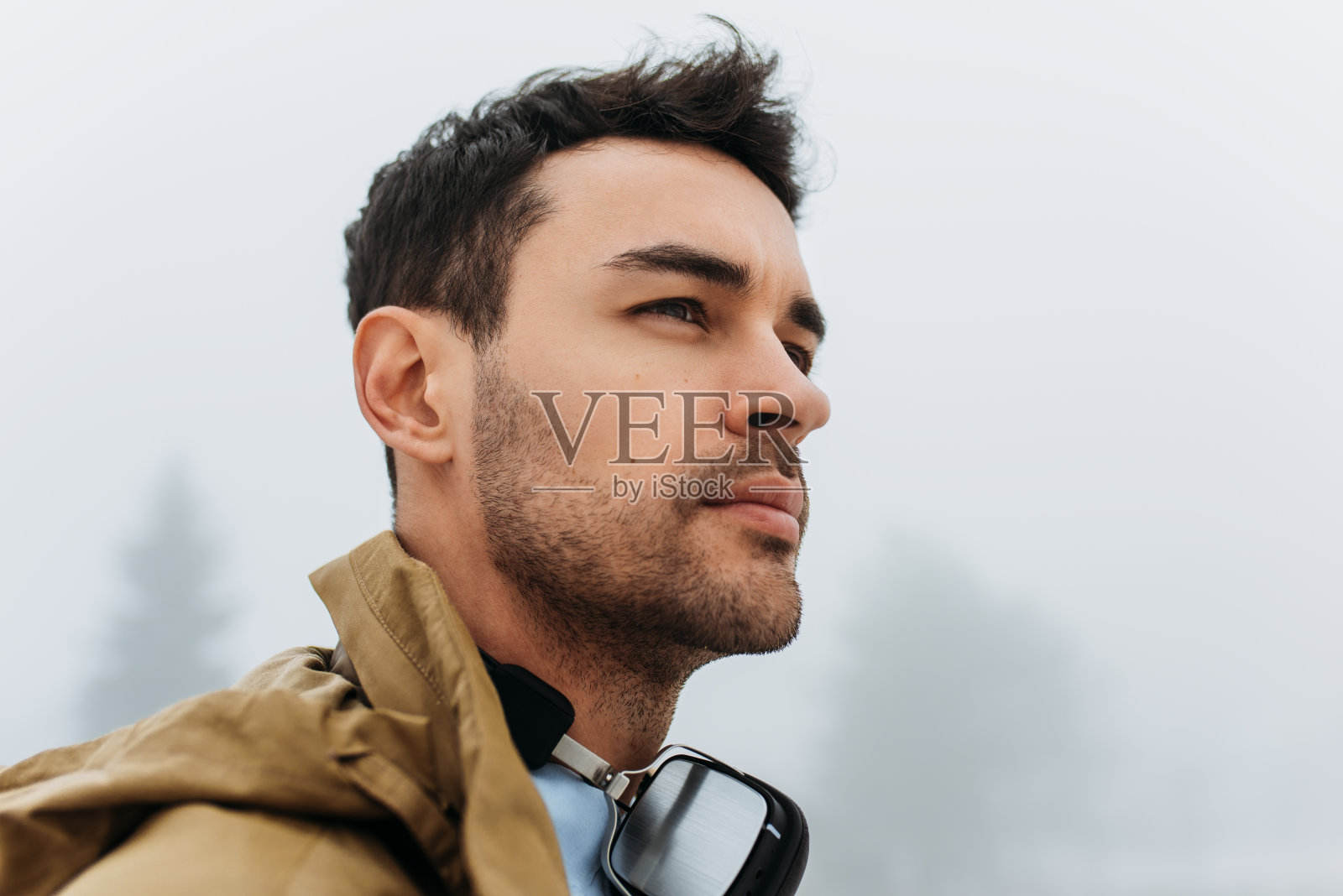 一个年轻人的特写肖像行走在一个雾天。旅行者男穿着外套，戴着耳机在山外听音乐。照片摄影图片
