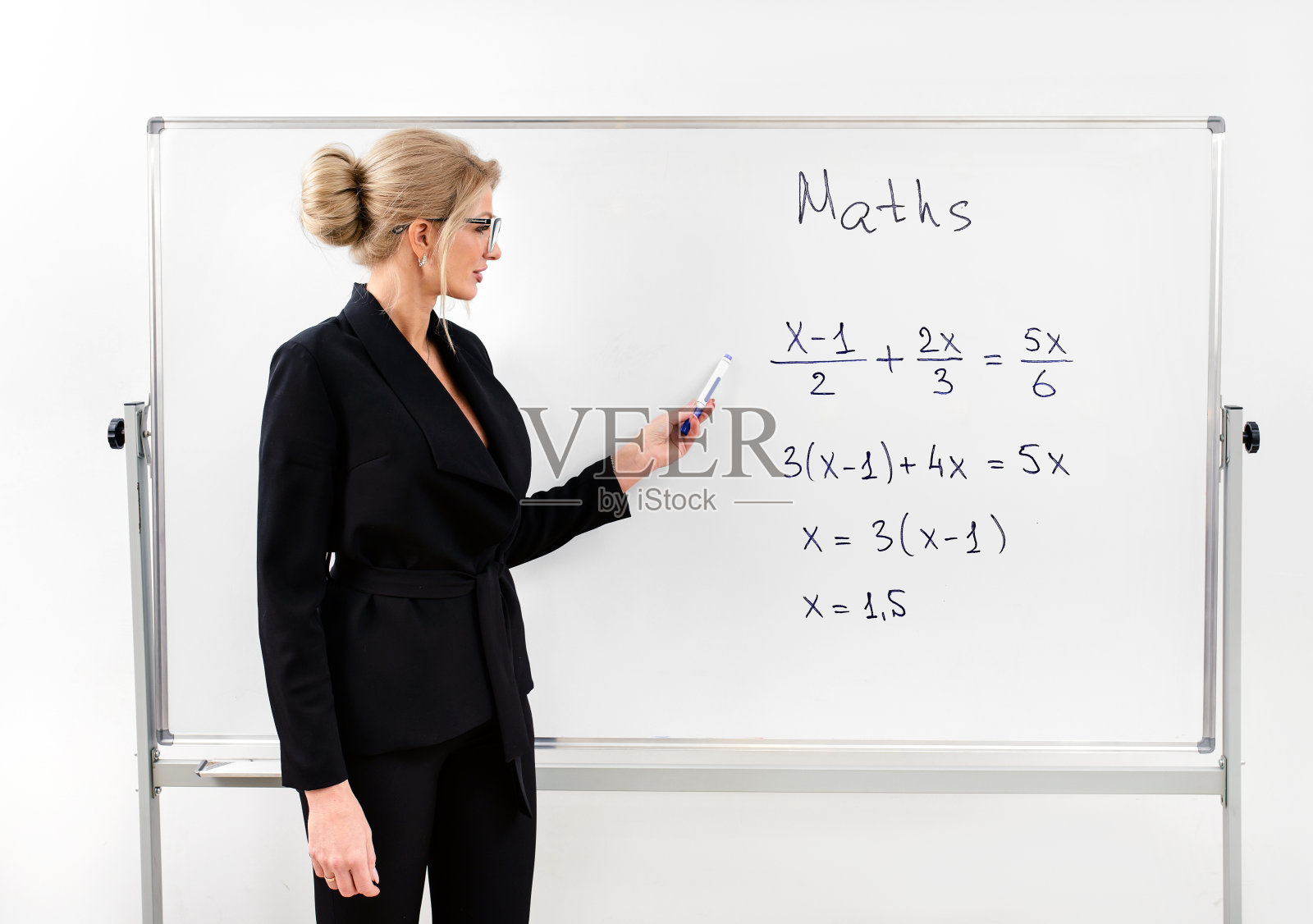 在现代教室里，一个穿着黑色套装的老师在白板旁边教数学。本空间照片摄影图片