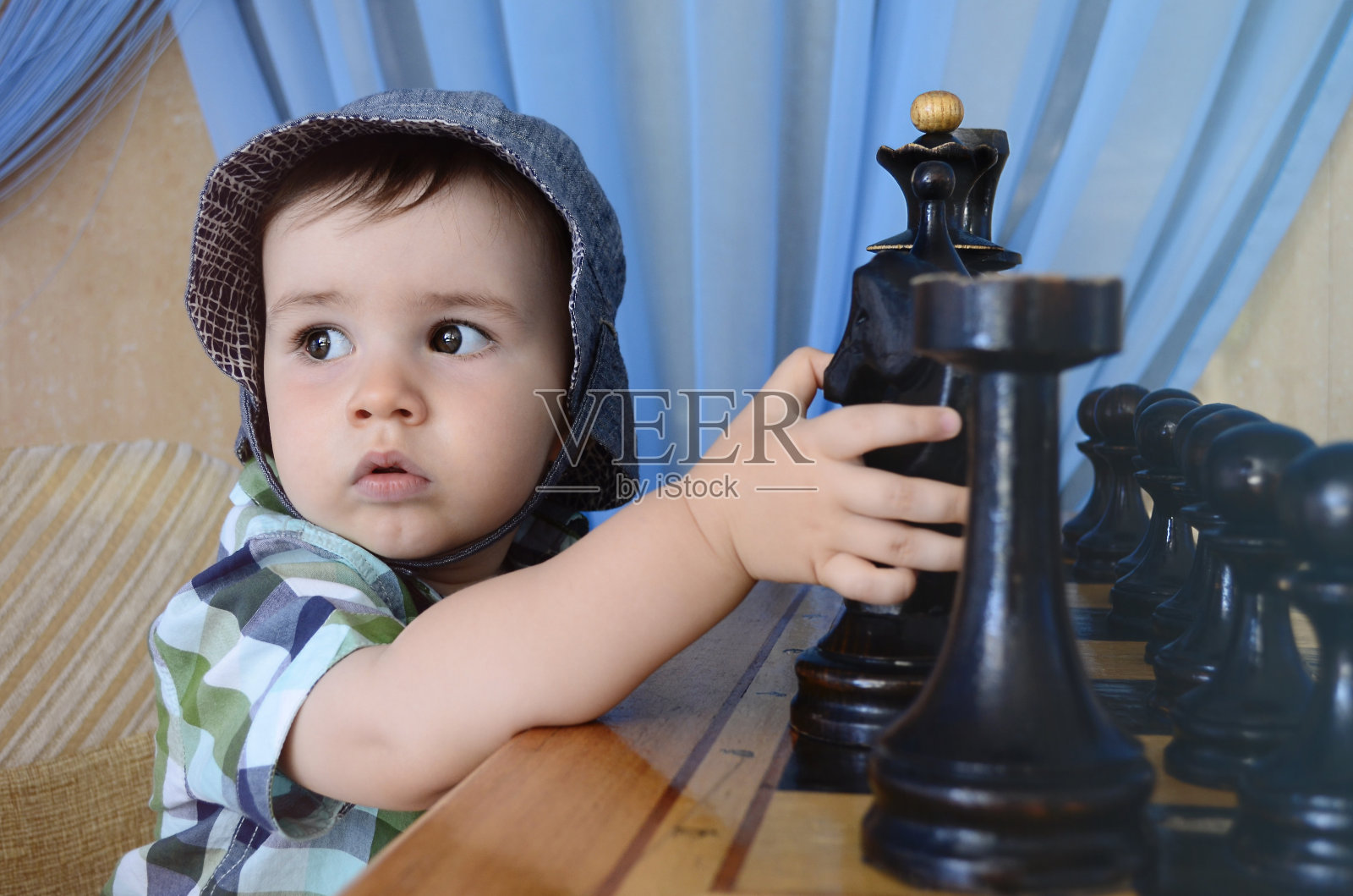 一个戴着帽子，眼睛严肃的孩子，看着旁边的象棋桌子上的数字，手拿着一匹马。照片摄影图片