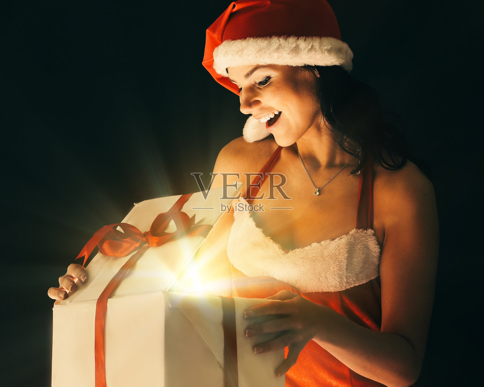 身着圣诞老人服装的年轻女子惊讶地打开了一份圣诞礼物照片摄影图片