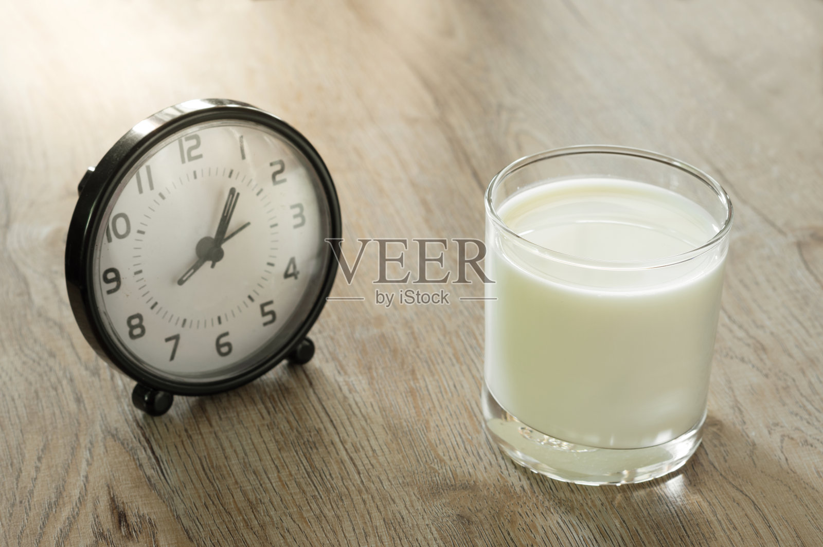 牛奶杯和闹钟放在木桌上。照片摄影图片