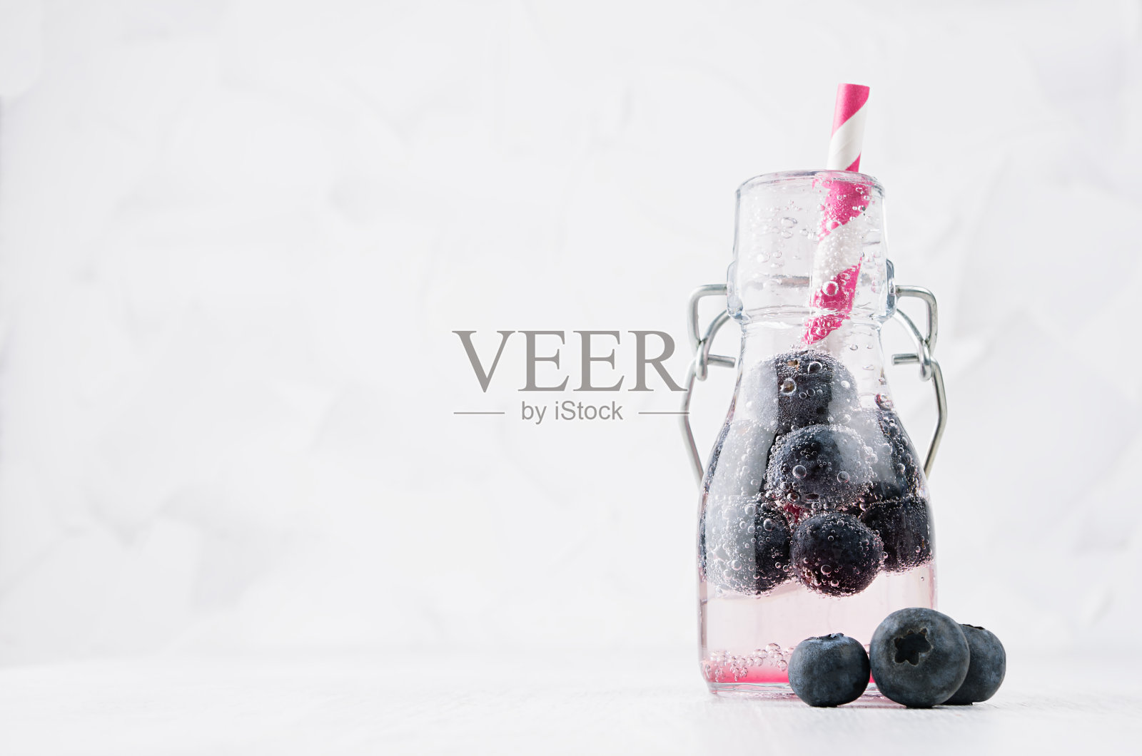 冷鲜水果粉色成熟蓝莓饮料与苏打水，气泡，有趣的条纹吸管在简单柔和明亮的白色背景，复制空间。照片摄影图片