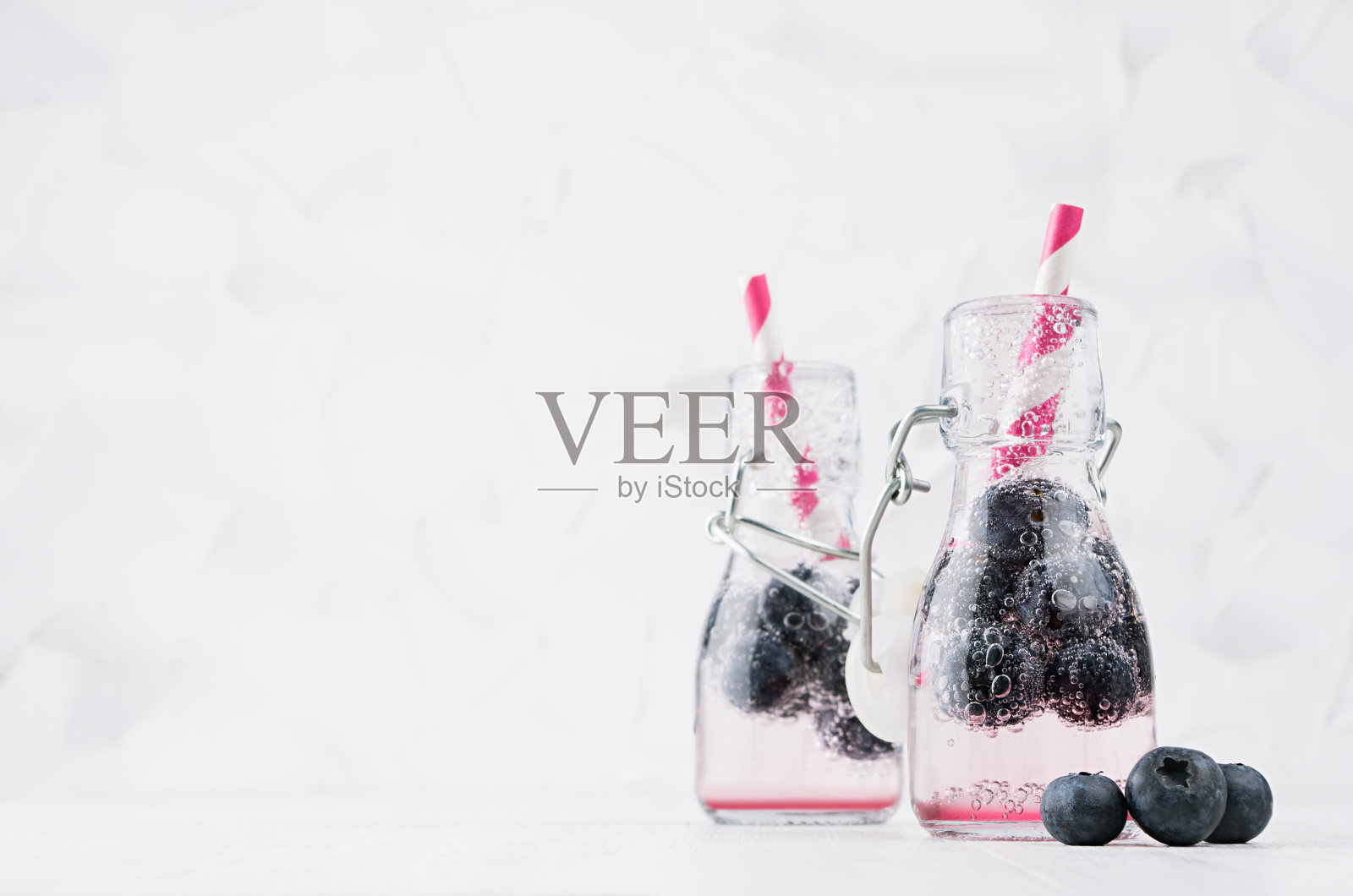 清新的冷果粉色饮料与蓝莓，明亮的气泡和吸管在透明的轭形瓶在优雅的白色内饰木桌子，复印空间。照片摄影图片