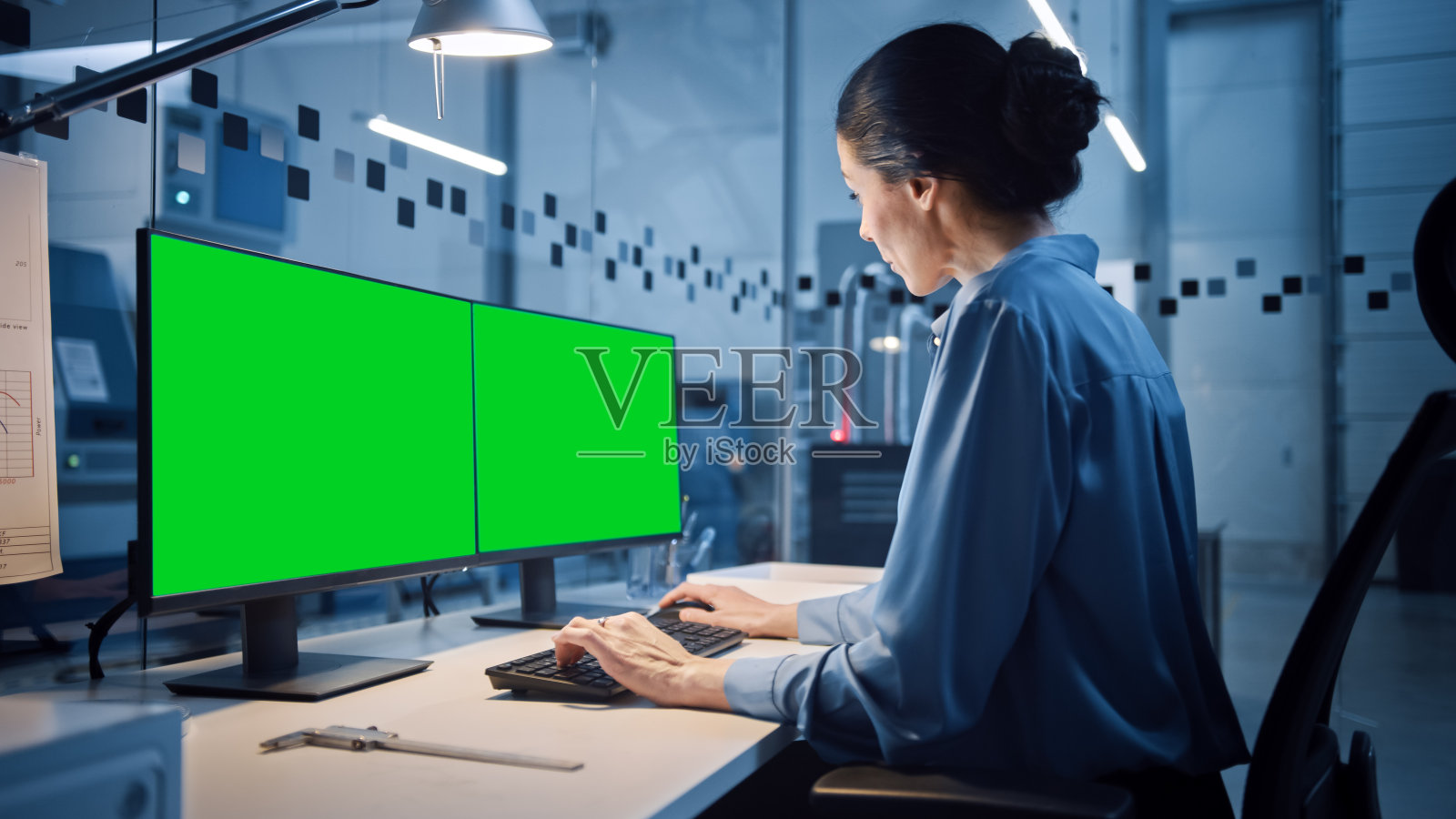 工厂办公室:美丽和自信的女性工业工程师的肖像工作在个人电脑与两个绿色屏幕色度键显示。配备数控机床的高科技设备照片摄影图片
