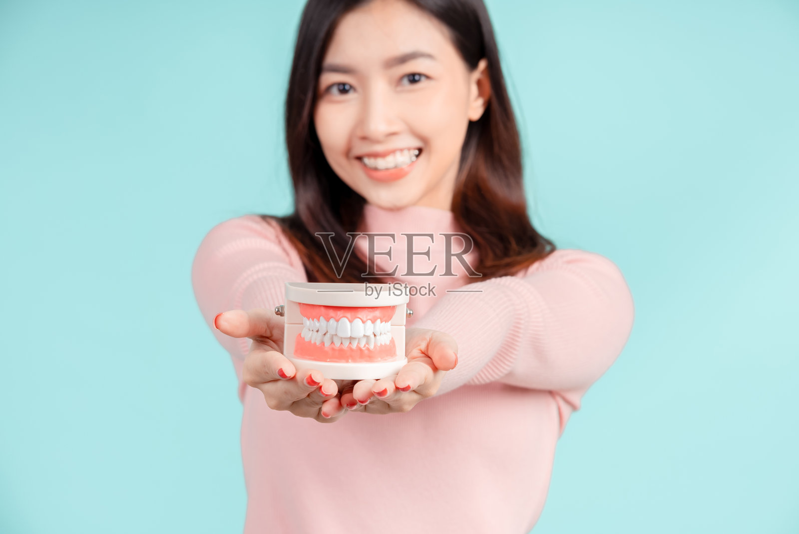 牙齿的亚洲妇女与牙齿样本和白色的牙齿增加信心为健康的蓝色背景孤立工作室拍摄，幸福的青少年微笑的面部表情。照片摄影图片
