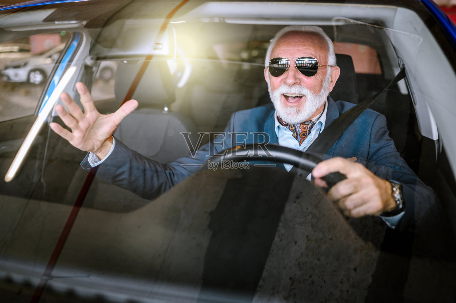 快乐的老人开着车，向别人挥手。照片摄影图片