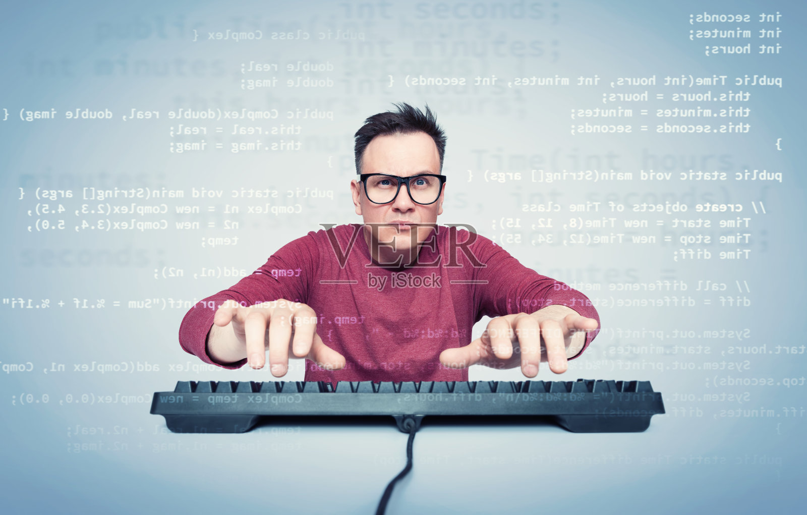 一个戴眼镜、穿红色t恤的男人的肖像，他在键盘上打字，看着显示器上的计算机代码。前视图。照片摄影图片