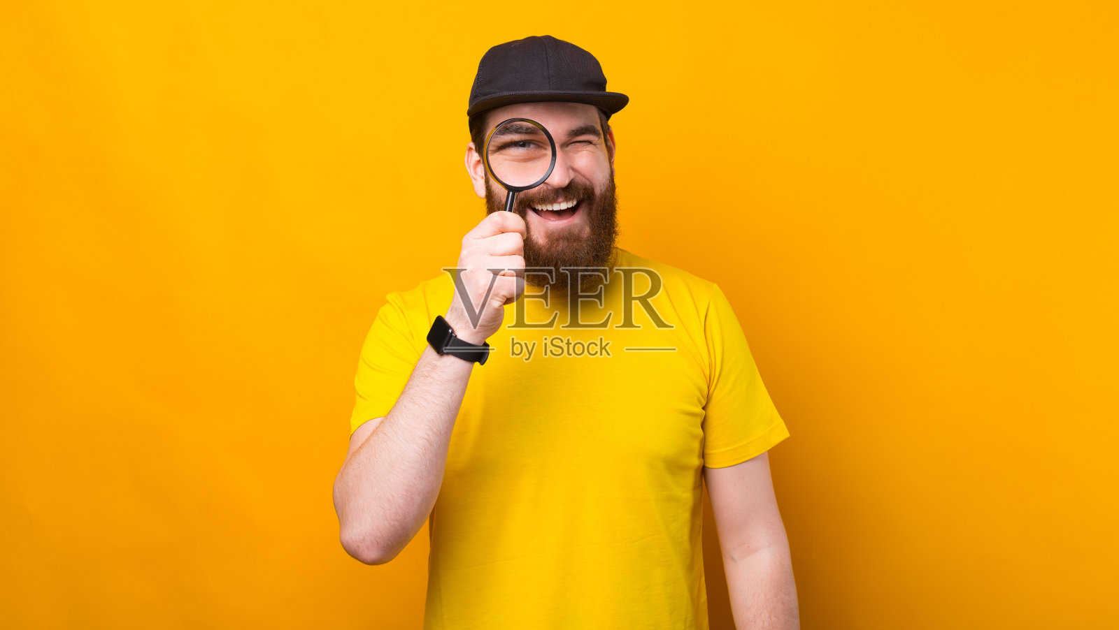 一个留着胡子的愉快的年轻人正在用放大镜看照片摄影图片