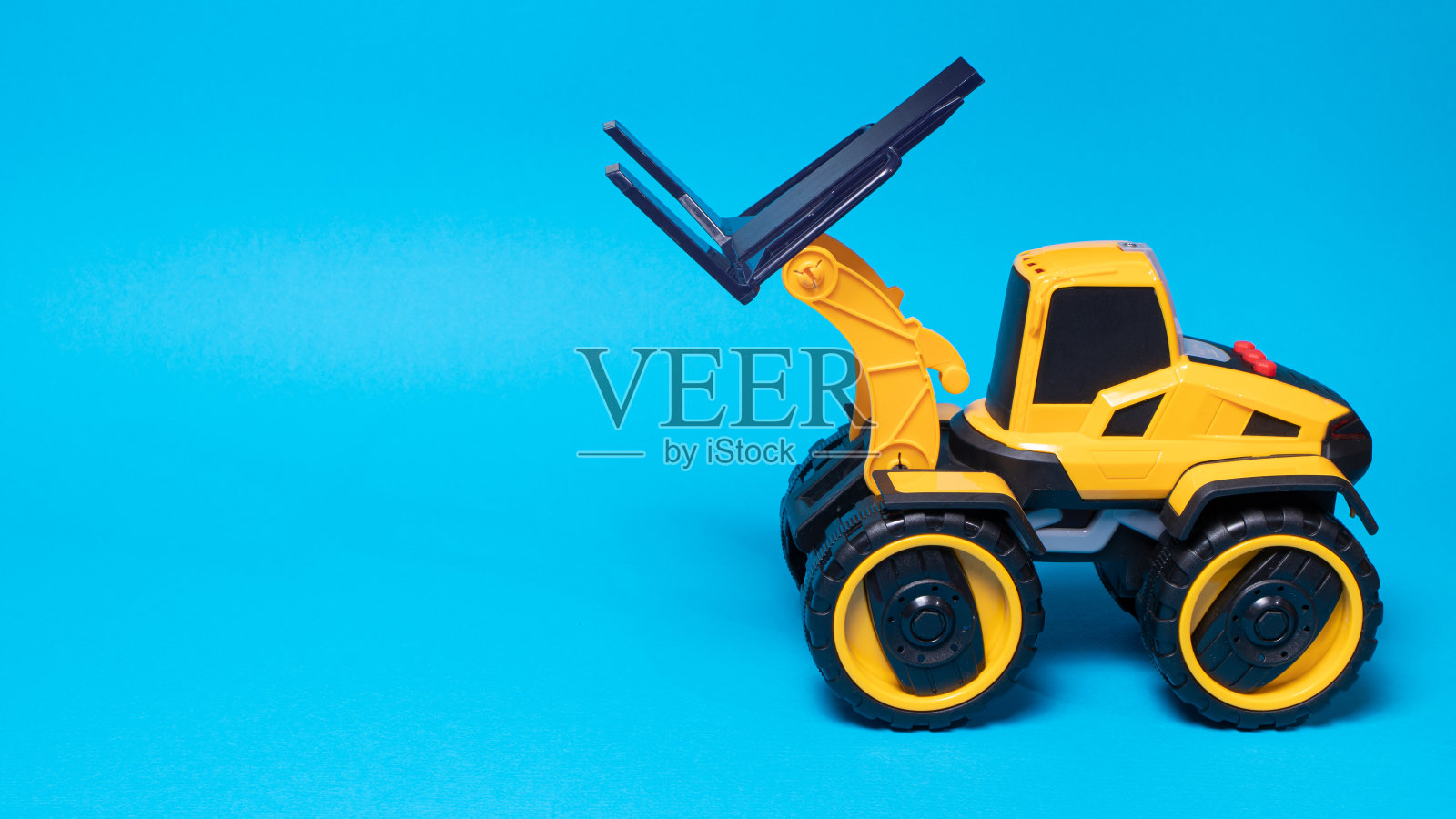 黄色的黑色叉车玩具打字机在一个蓝色的背景。建筑设备拖拉机儿童为玩具店，copyspace为文本的地方照片摄影图片