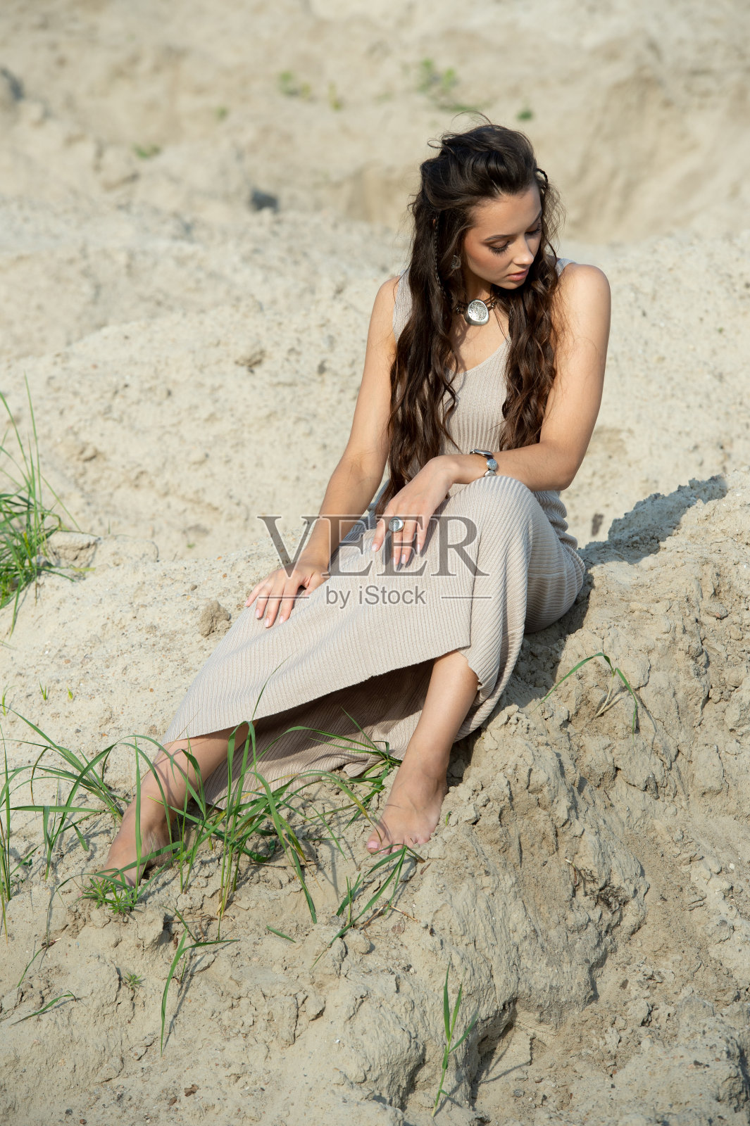 夏天的时候，在海滩上晒太阳的女人度假。快乐的女人穿着夏装坐在沙滩上看海。是时候放松在夏天的生活方式户外拍摄的岛屿海滩照片摄影图片