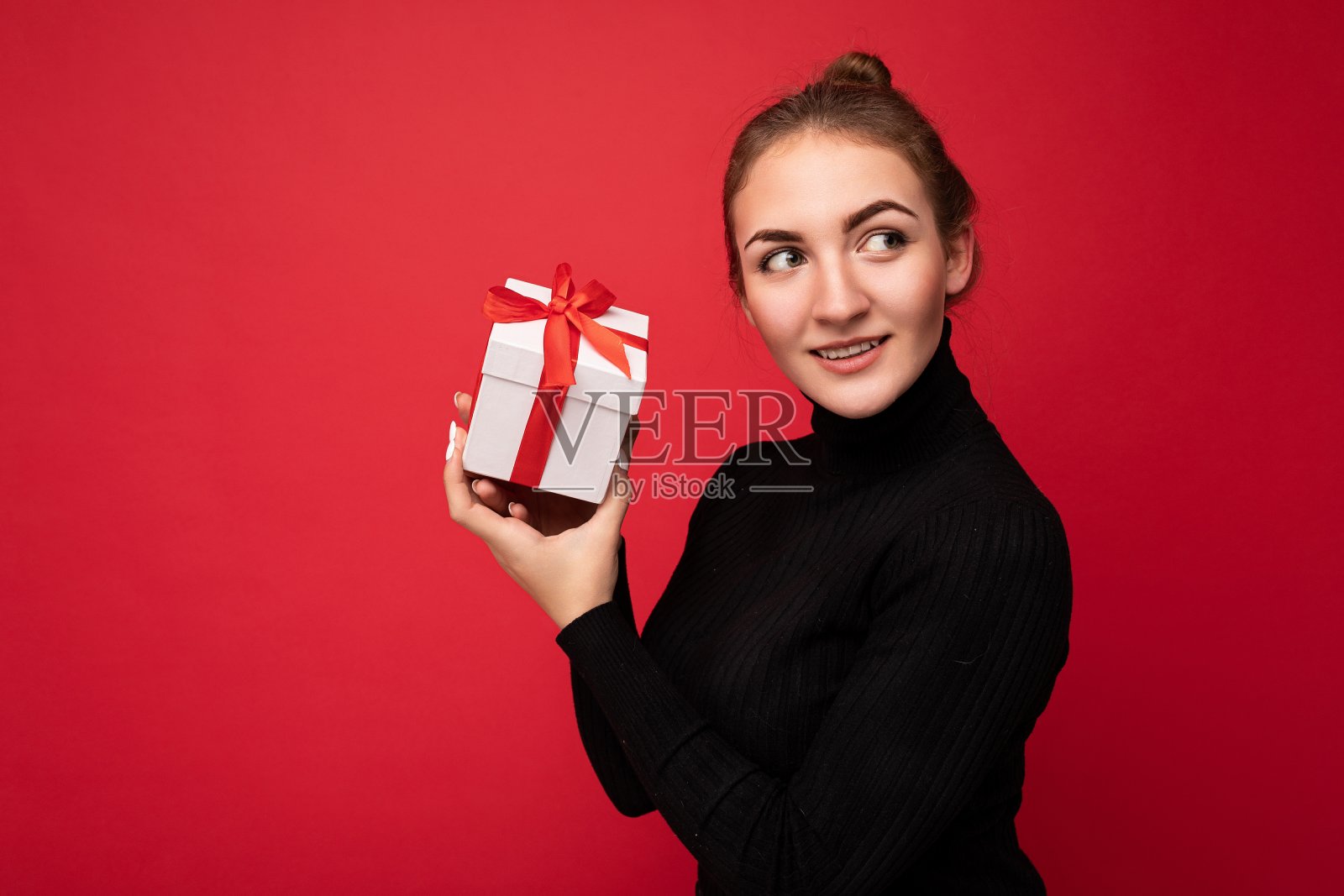 吸引人的正面微笑年轻的黑发女子孤立在色彩鲜艳的背景墙穿着日常时尚的服装拿着礼盒和看向一边照片摄影图片