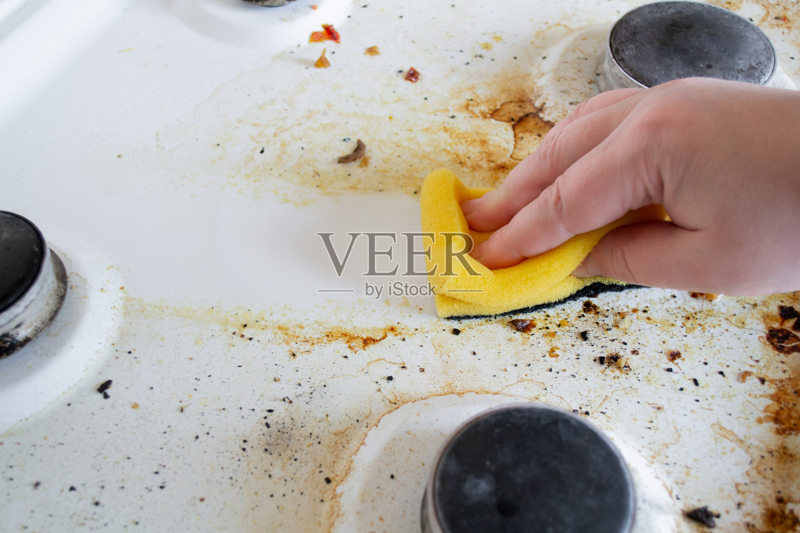 一只手用黄色的洗涤海绵清洗煤气炉非常脏油腻的表面。海绵擦拭后，会留下干净的痕迹照片摄影图片