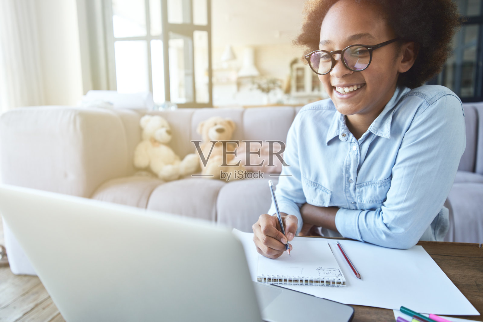 快乐的混血女孩戴着眼镜微笑着做作业，用笔记本电脑，在起居室学习期间在家隔离照片摄影图片