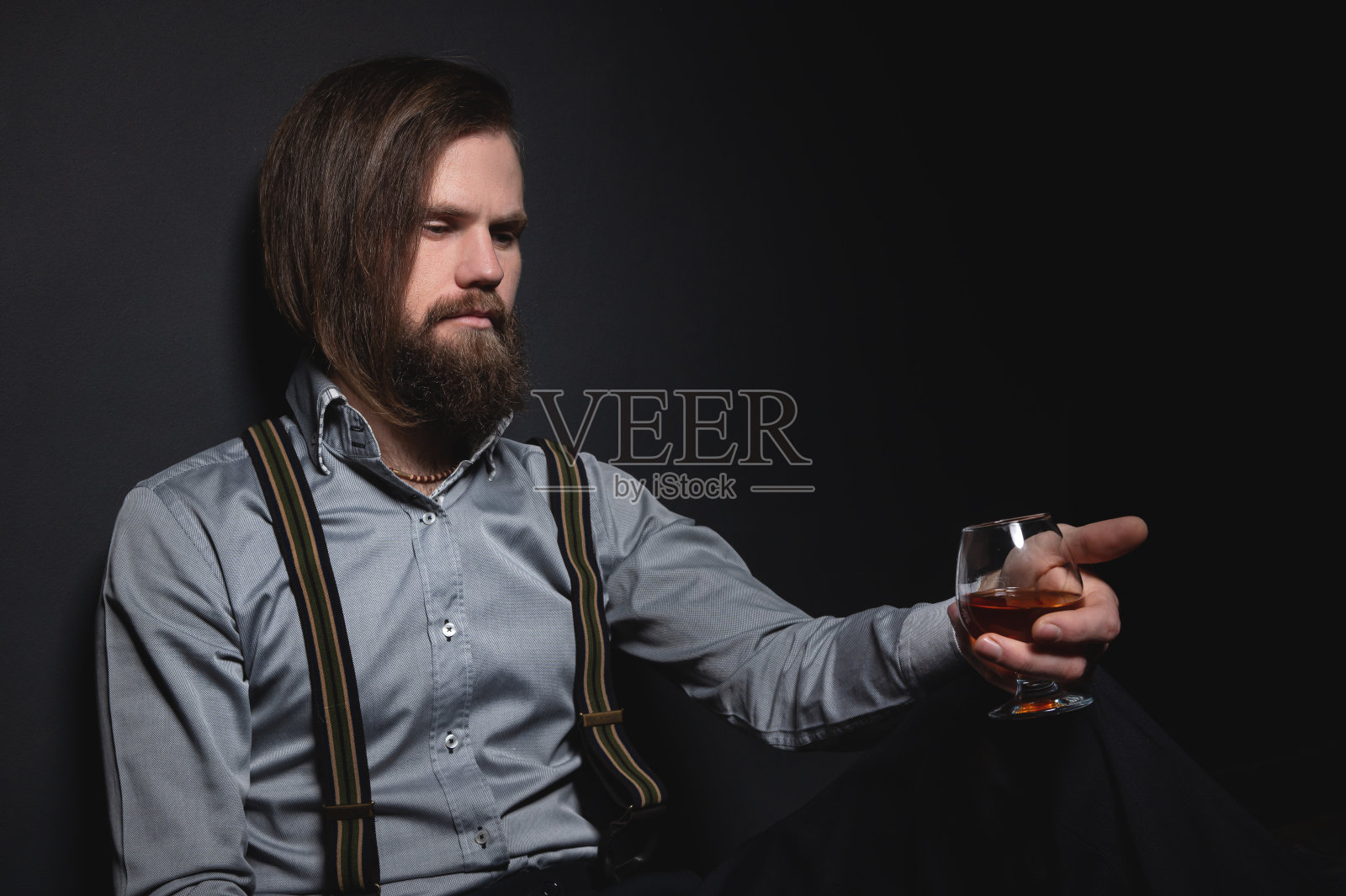 有胡子的男人拿着白兰地酒杯。大胡子喝白兰地。侍酒师口味的饮料。拿着一杯威士忌的男人。喝威士忌。照片摄影图片