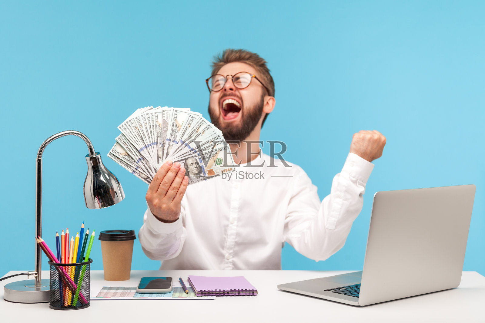 一名极度快乐的白领手里拿着一大笔钱尖叫着，中了彩票坐在办公地点用笔记本电脑照片摄影图片
