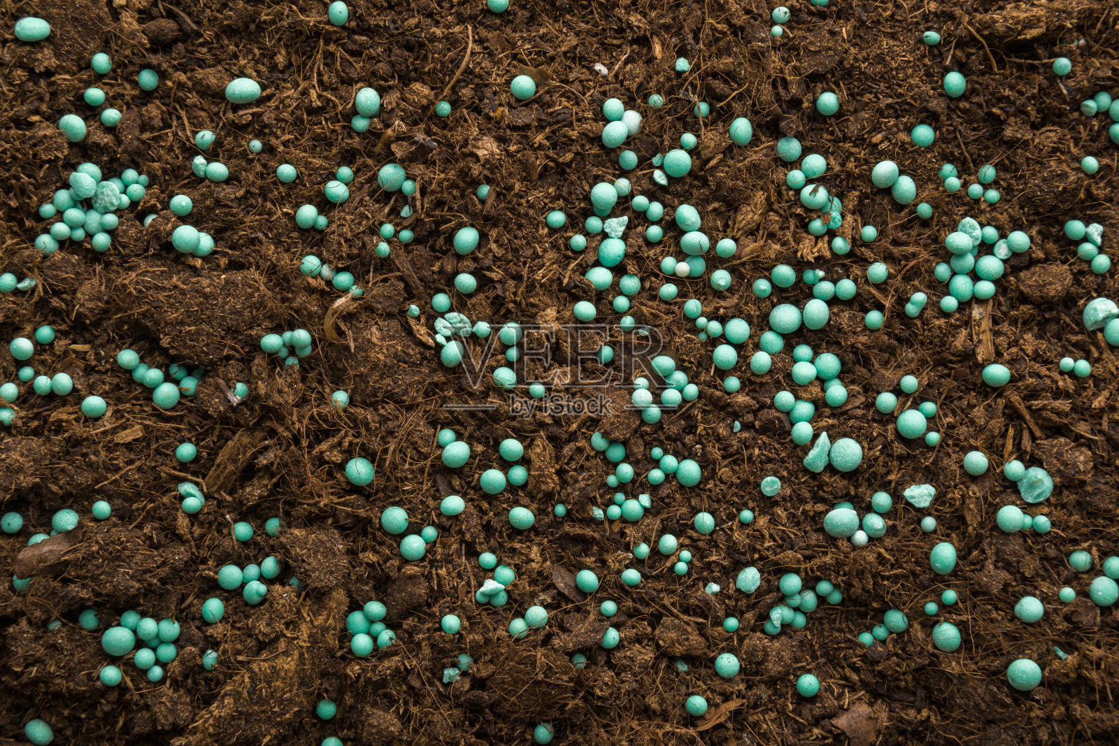 深褐色土壤上的绿色复合肥料颗粒。特写镜头。产品适用于蔬菜、花卉、植物的根饲。自顶向下的观点。照片摄影图片