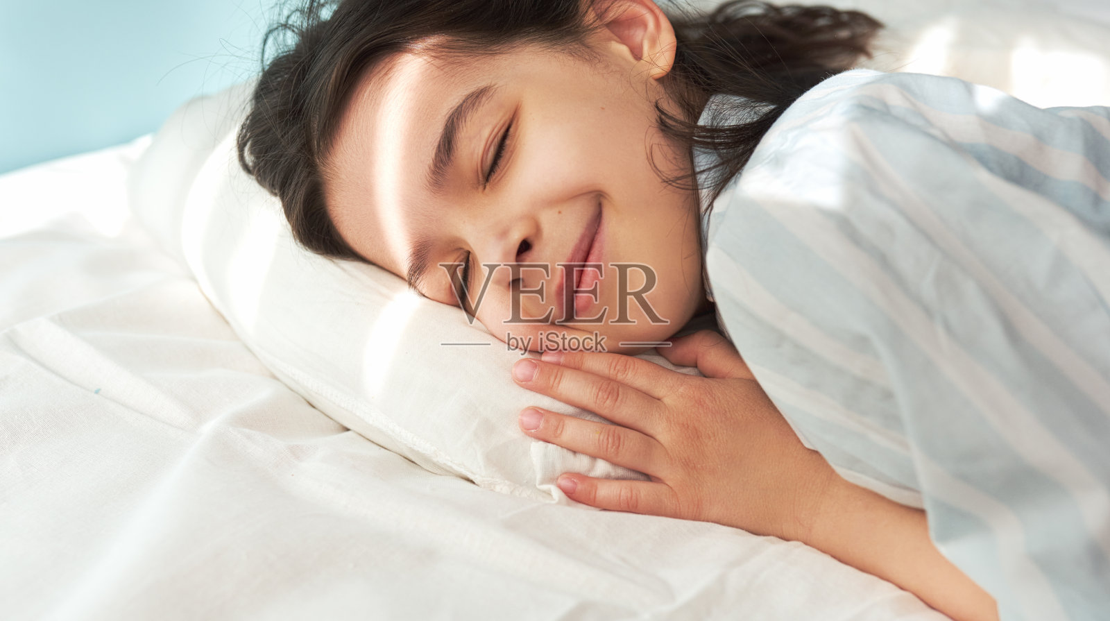 一个可爱的小女孩清晨睡在床上的特写。在家里舒适的白色床上休息和微笑的可爱的孩子。照片摄影图片