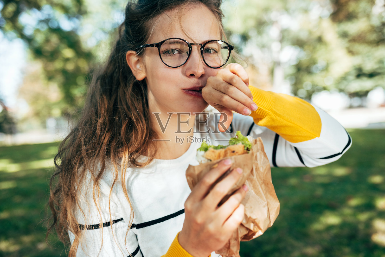 一个女学生的肖像有一个美味的午餐和一个三明治在户外。一位戴眼镜的金发年轻女子在公园里休息吃快餐。照片摄影图片