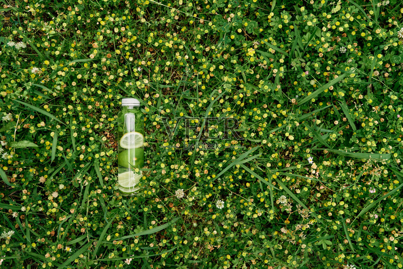 一瓶柠檬水躺在黄色的野花中间的绿色草坪上照片摄影图片