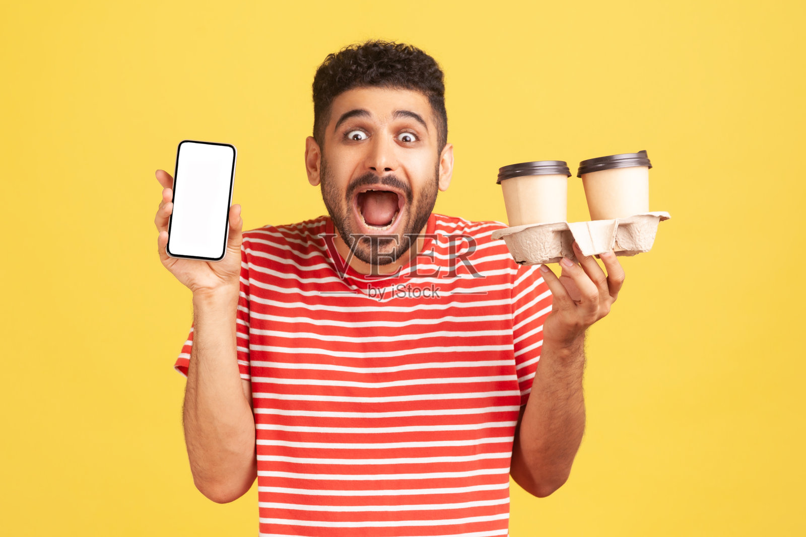 一名身穿条纹t恤的大胡子男子震惊地尖叫着，手里拿着白色显示屏的智能手机和两个装着咖啡的纸杯，惊讶于快递速度之快照片摄影图片