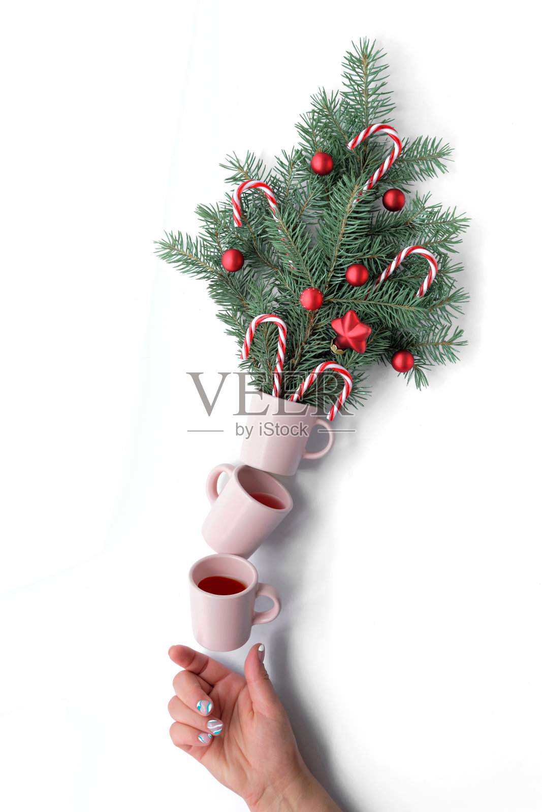 创造性的圣诞平衡安排。咖啡杯支撑着花盆，花盆上装饰着红色的圣诞装饰物和拐杖糖。手支撑着金字塔。创意的圣诞布置照片摄影图片
