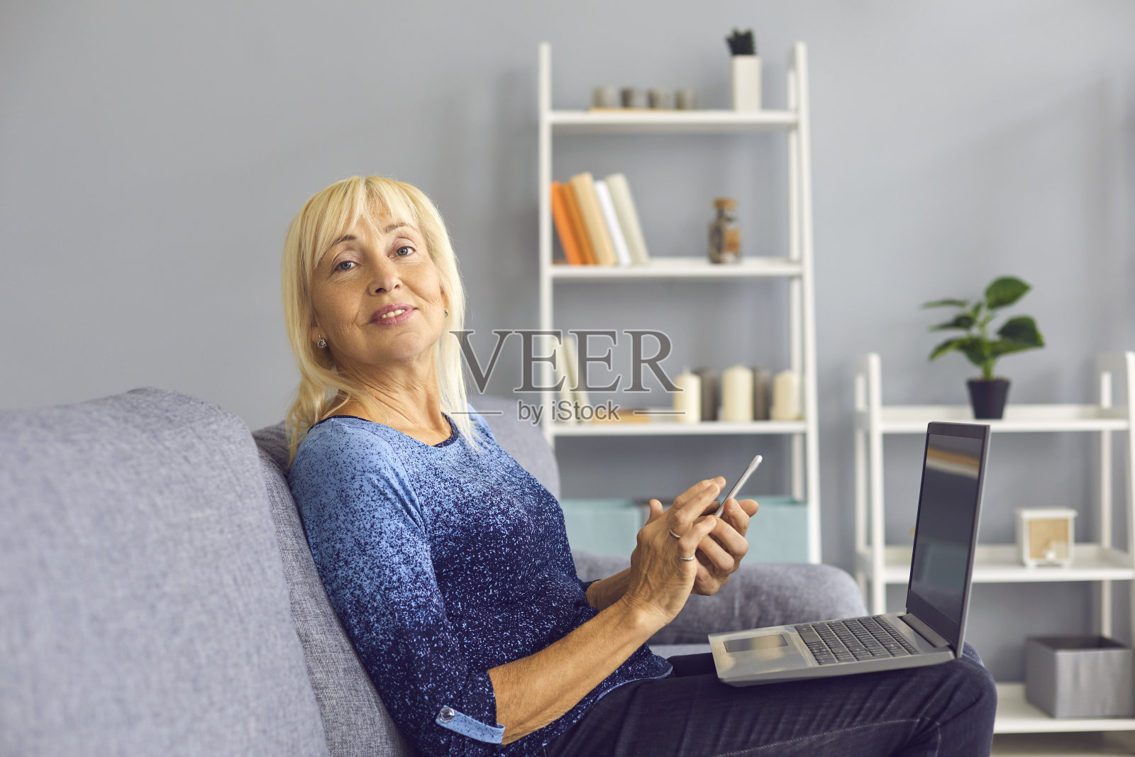 一个成熟的女人坐在沙发上，拿着笔记本电脑，拿着手机，看向别处照片摄影图片