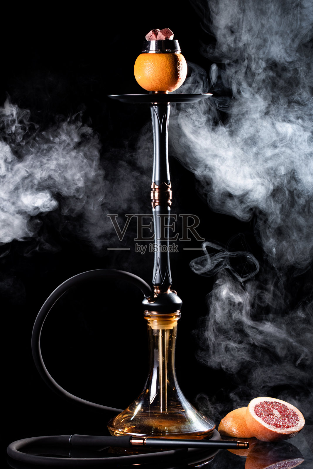 水烟水烟与玻璃烧瓶和水果葡萄柚碗与白色烟在黑色的背景。传统的东方放松照片摄影图片