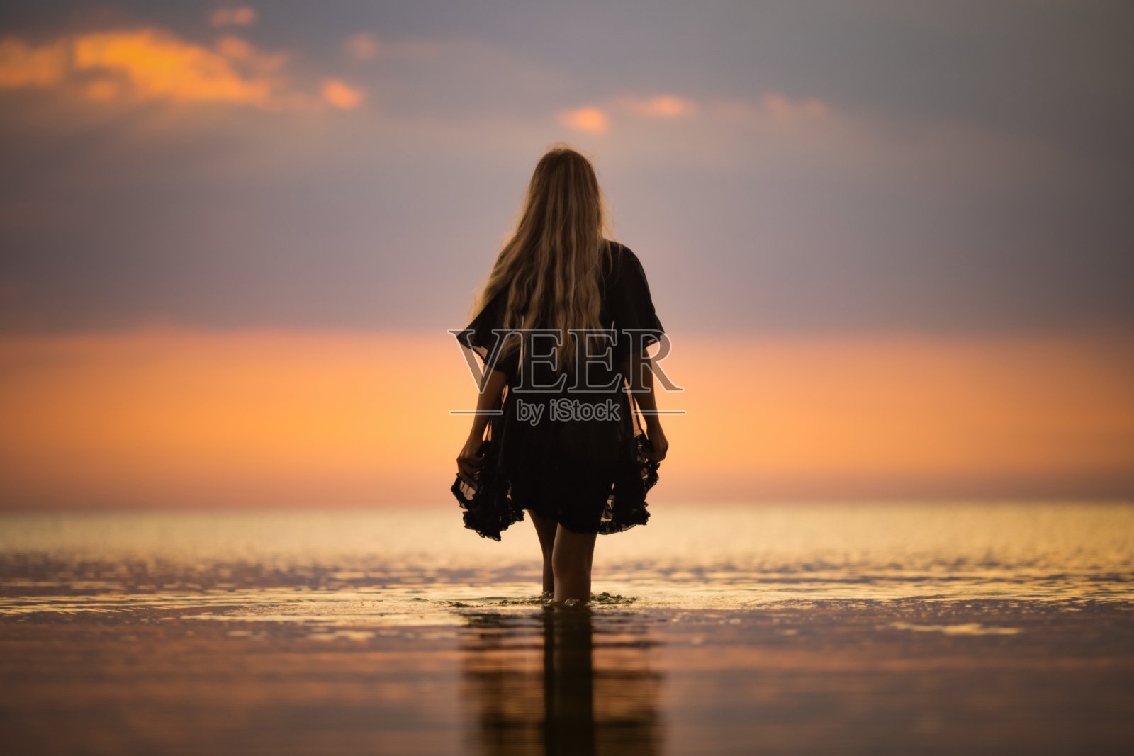 一个金发碧眼的女孩穿着黑色比基尼，披着蕾丝披肩，沿着河口走着照片摄影图片