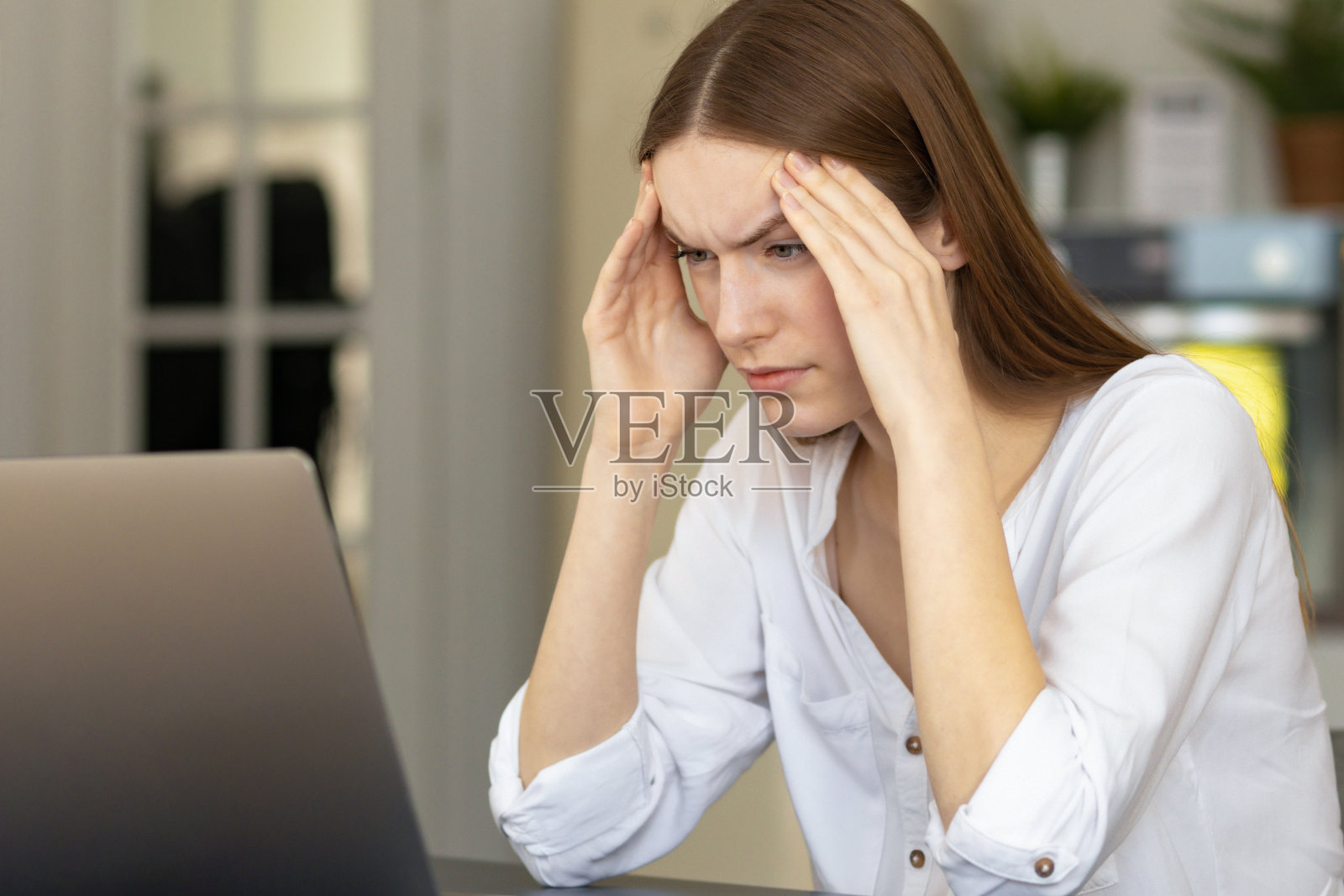 疲惫的白人女商人头痛或偏头痛坐在办公室办公桌。年轻的女性自由职业者坐在家里的办公室忍受着电脑上的过度工作照片摄影图片