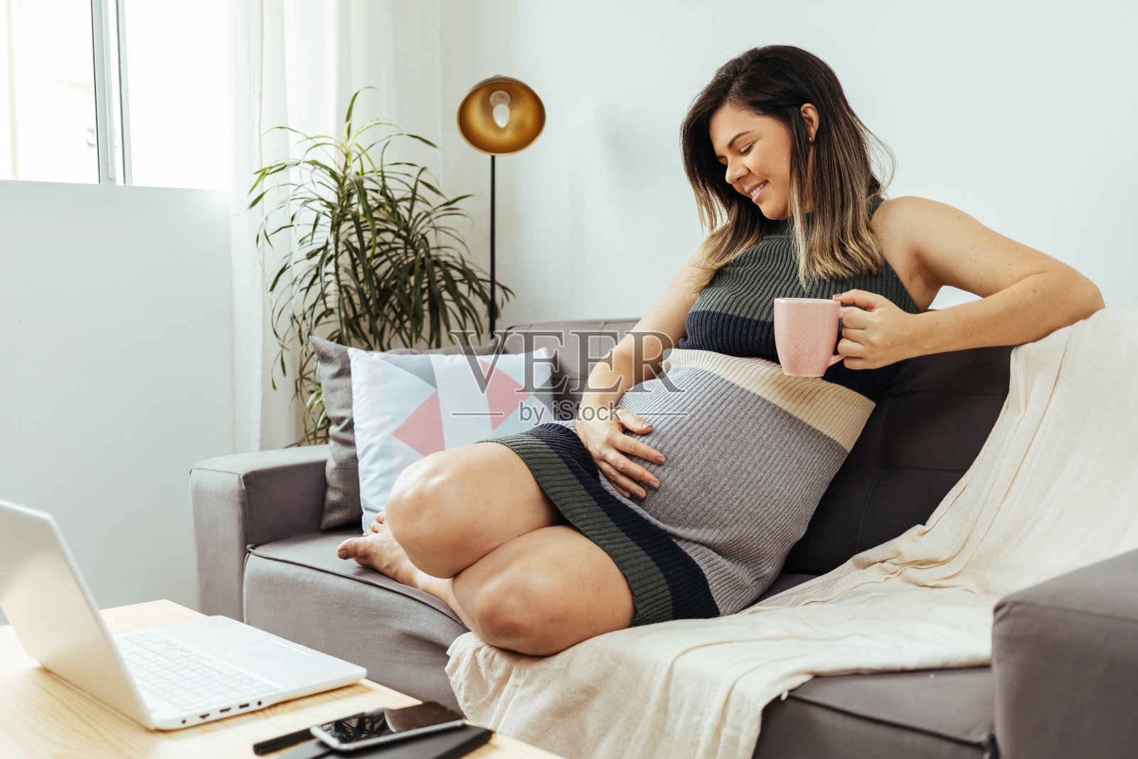 孕妇坐在沙发上用笔记本电脑。孕妇在家工作的概念照片摄影图片