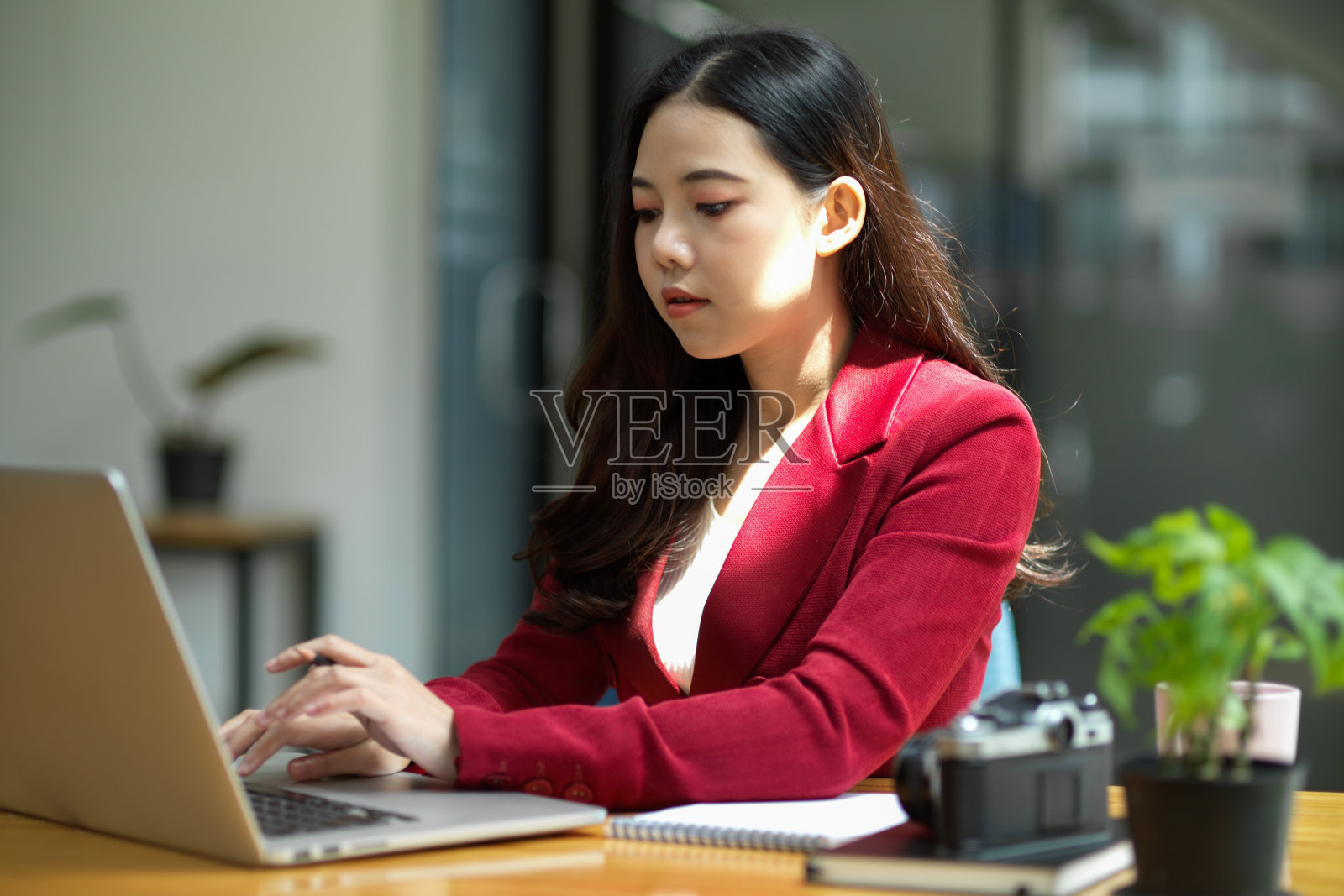 在一间明亮的现代办公室里，一位女商人坐在她的办公桌前，用笔记本电脑工作。照片摄影图片
